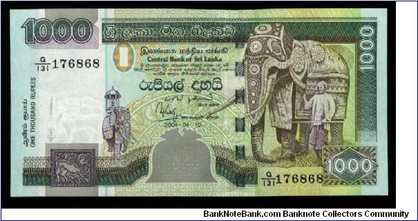 1,000 Rupees.

Chinze at lower left, two-heaaded bird at bottom center, elephant with trainer at right on face; peacocks on palace lawn, lotus flowers above and Octagon of Temple of the Tooth in Kandy on back.

Pick #NEW Banknote